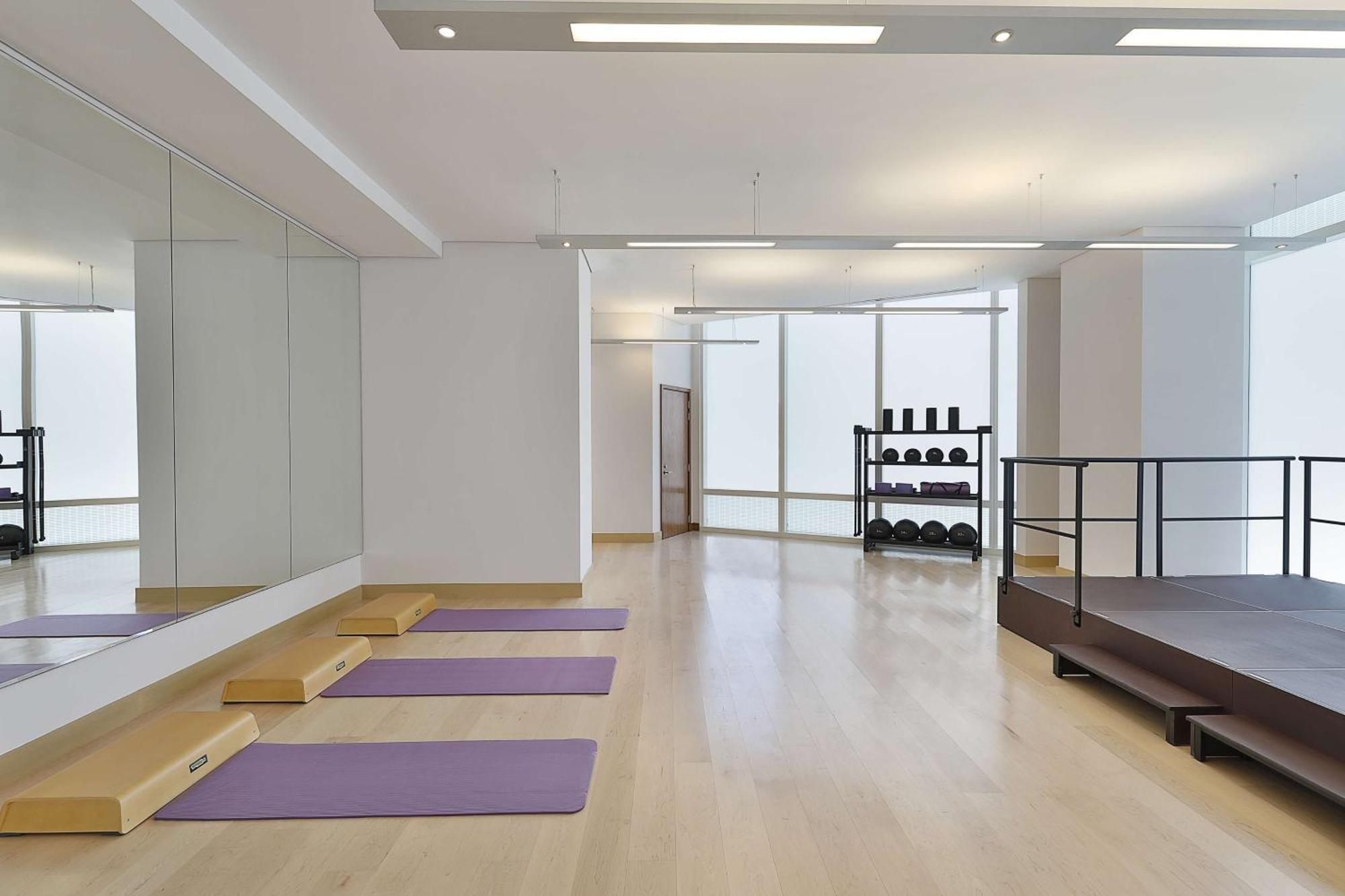 Hilton Riyadh Hotel & Residences Εξωτερικό φωτογραφία The photo depicts a spacious exercise or workout studio. It features wooden flooring and a large mirror on one wall. There are three purple yoga mats neatly placed on the floor, and a small set of wooden steps beside them. In the background, there is
